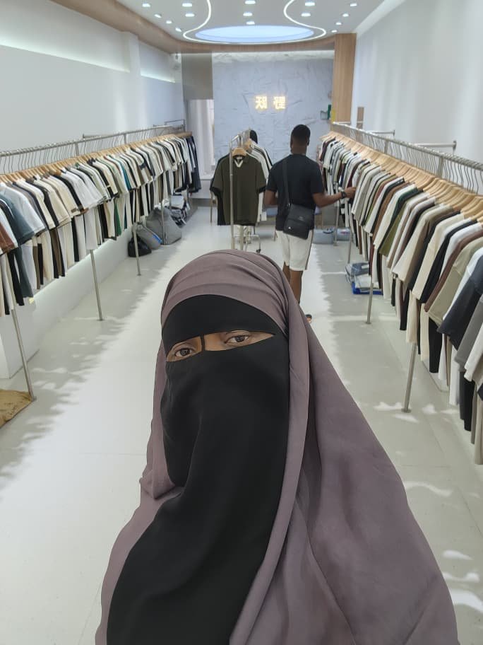 How to Find a Reliable China Agent in Nigeria (and What to Ask Before You Pay) A woman in a veil standing in a clothing wholesale shop with racks of garments behind her