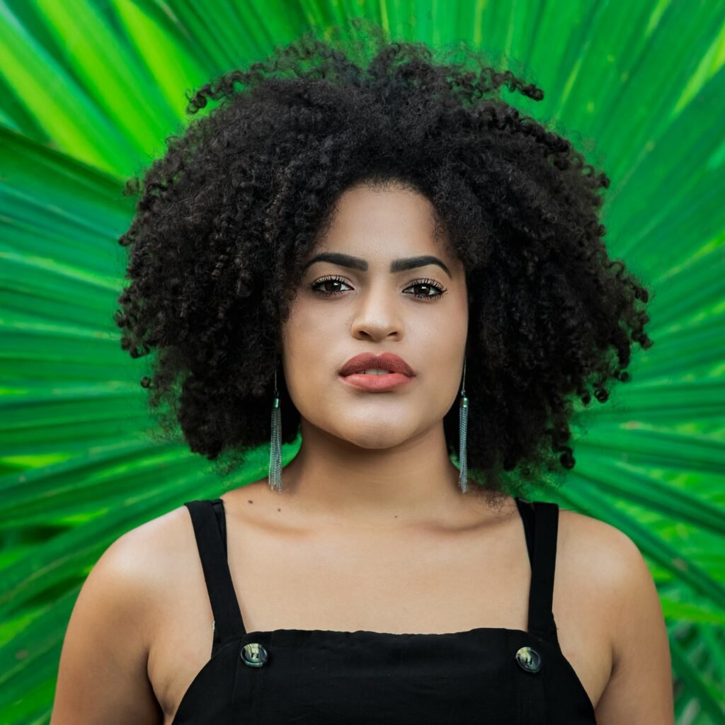 Striking portrait of a woman with curly afro hair set against lush green leaves. Nature meets beauty.