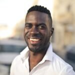 Portrait of a smiling man in a white shirt standing outdoors on a sunny day.