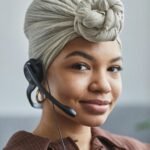 Smiling black woman in a head wrap and headset working in a call center.