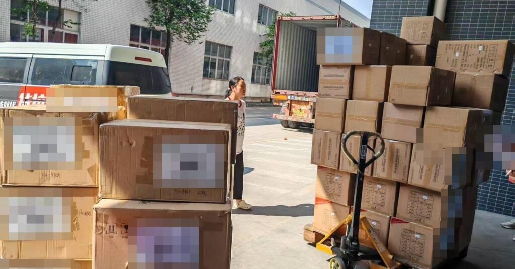 Boxes of goods stacked on pallets beside a container being loaded at a warehouse